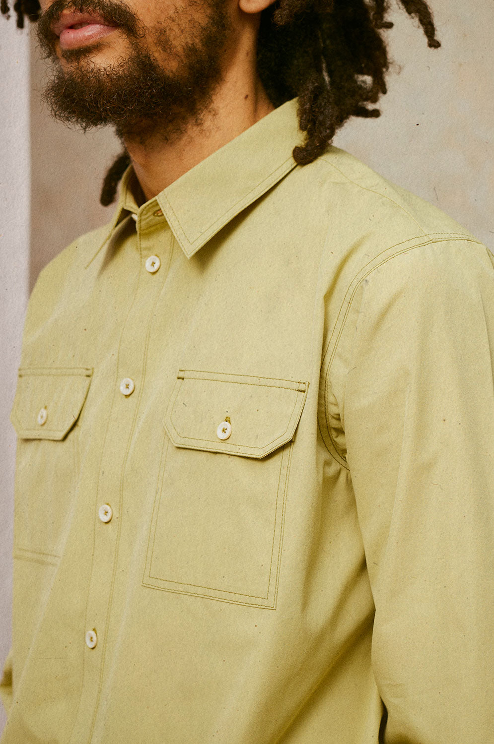 Close up of the Eddy Men's khaki Utility shirt, showing the chest and shoulders. The utility pocket on the chest, the collar and button placket, and top stitching detail can be seen clearly.