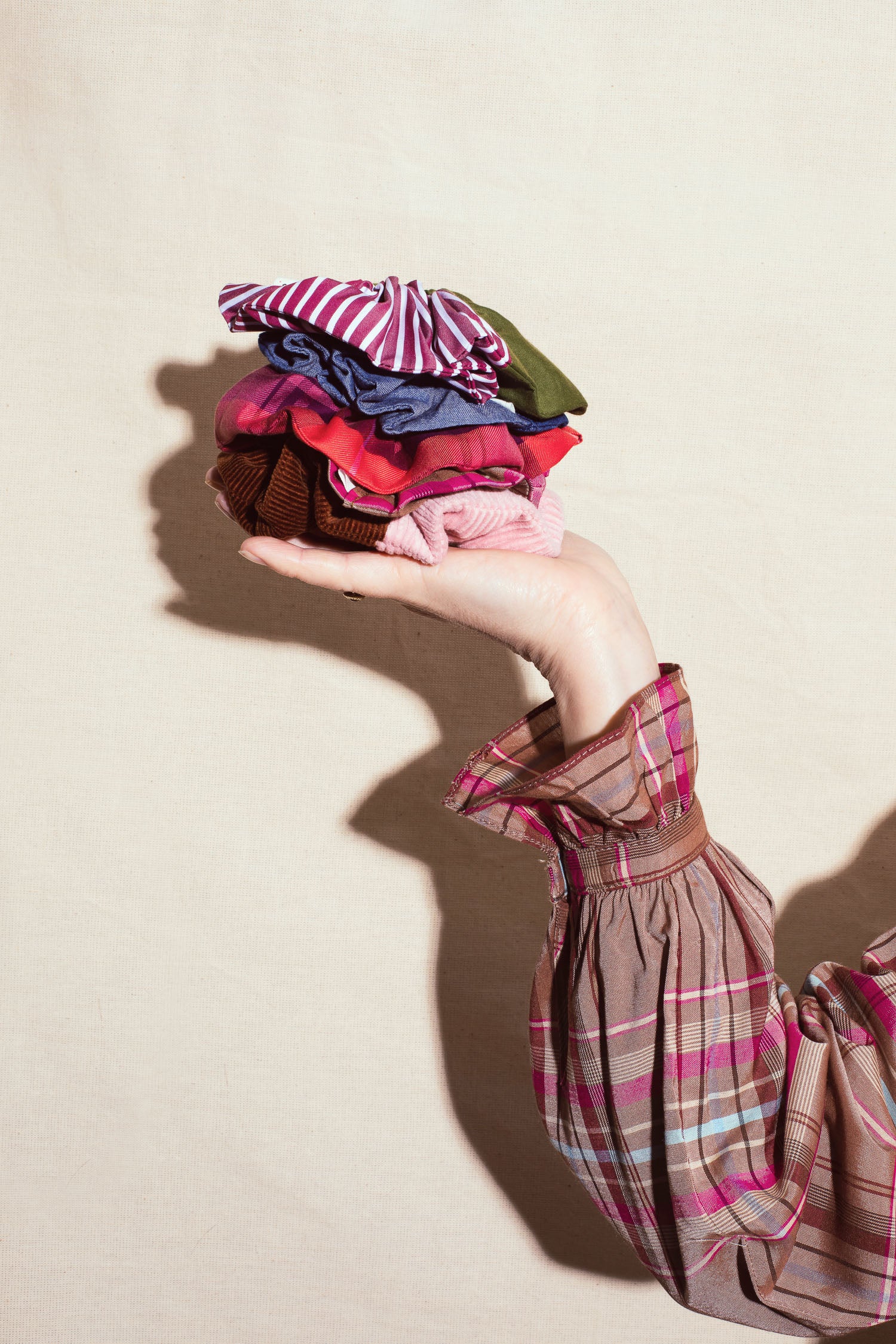 Person holding a stack of colorful fabric scrunchies against a beige background