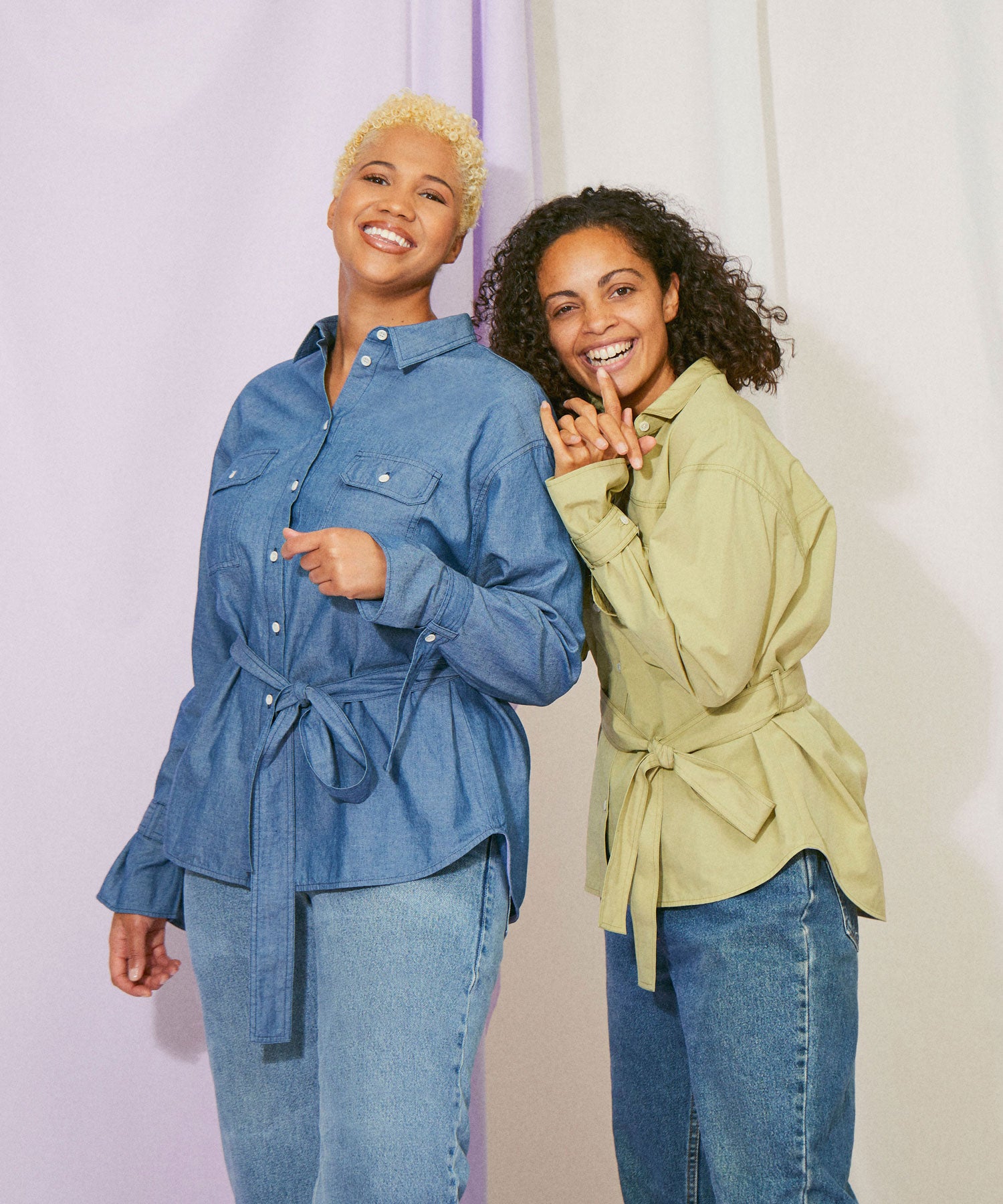 Two women stand next to each other laughing. The women on the left wears the Zadie Boyfriend Shirt in Japanese denim. The women on the right wears the same oversized shirt in olive khaki colour, and leans on the shoulder of the other woman.