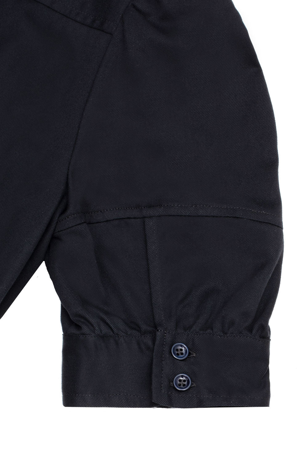 Close up of the back of the puff sleeve on the Rosa Puff Sleeve Shirtdress in black Japanese denim. Two deep blue buttons can be seen on the cuffs. The image is a flat shot on a what background.