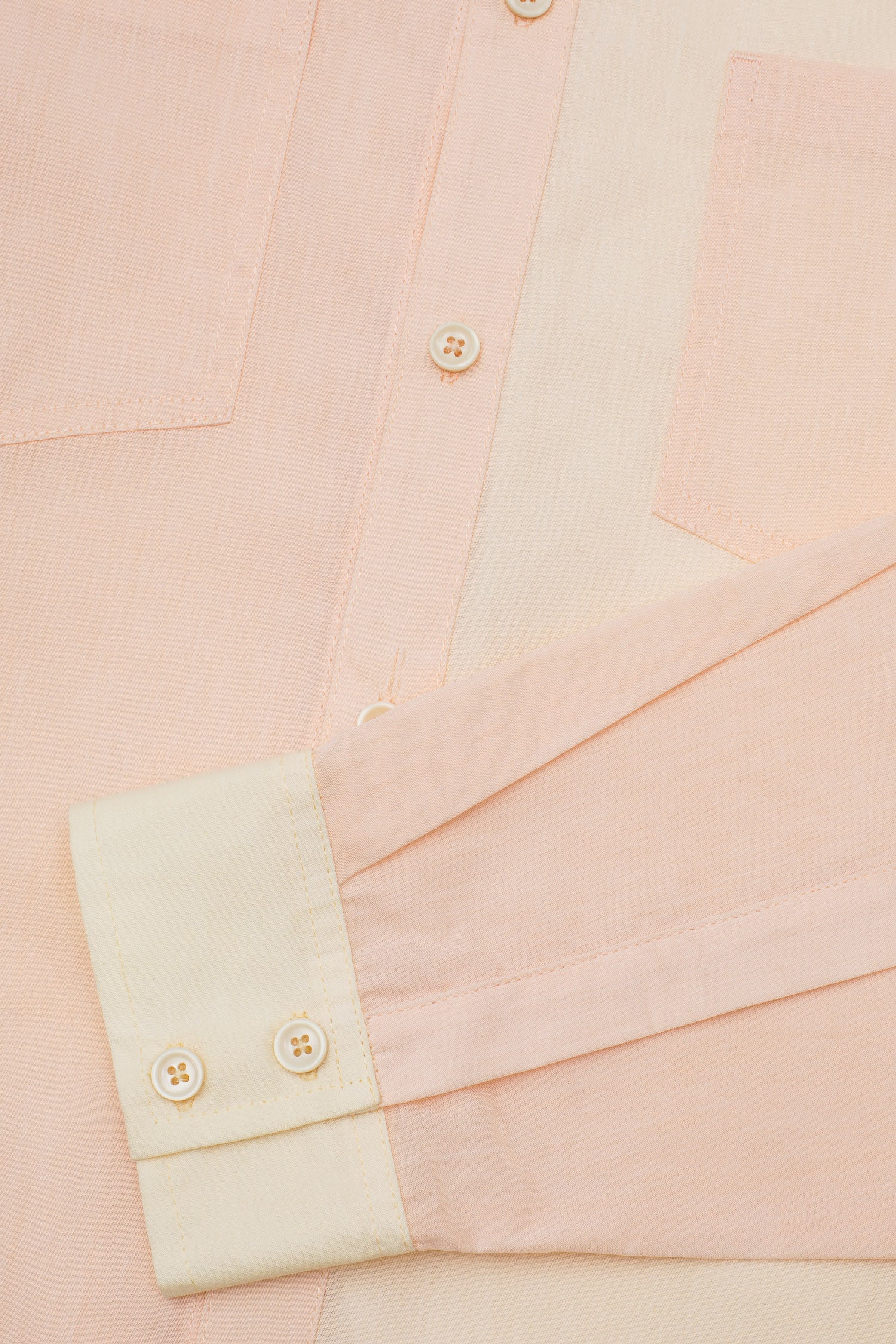Close up of the details of the Eddy Men's Colourblock Shirt in orange and pale yellow patchwork, showing the button placket, topstitched pocket edges and contrast cuff, with creamy natural Codelite buttons.