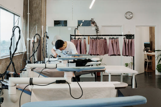 MAES London's Tottenham factory where they manufacture Saywood. A man can be seen pressing a garment on the ironing board, with Saywood's Bessie A-line Shorts in red stripe hanging in the background on a rail.