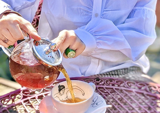 Yuyun Tea being poured from a glass tea pot into a tea cup. Founder of Yuyun wears Saywood Edi Shirt in White, with gathering details visible.