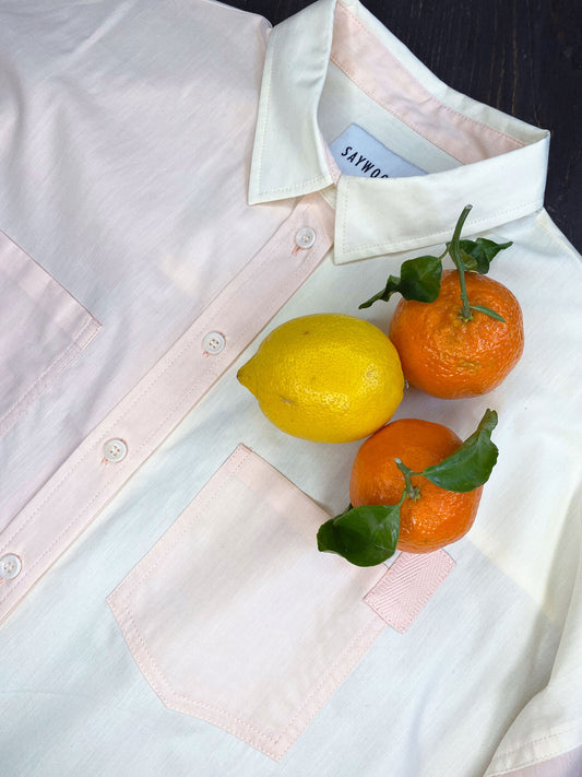 Saywood's pastel orange and lemon Lela Shirt, laid on a table, showing the upper body only, with clementines and lemon fruits lying on top of the shirt. 