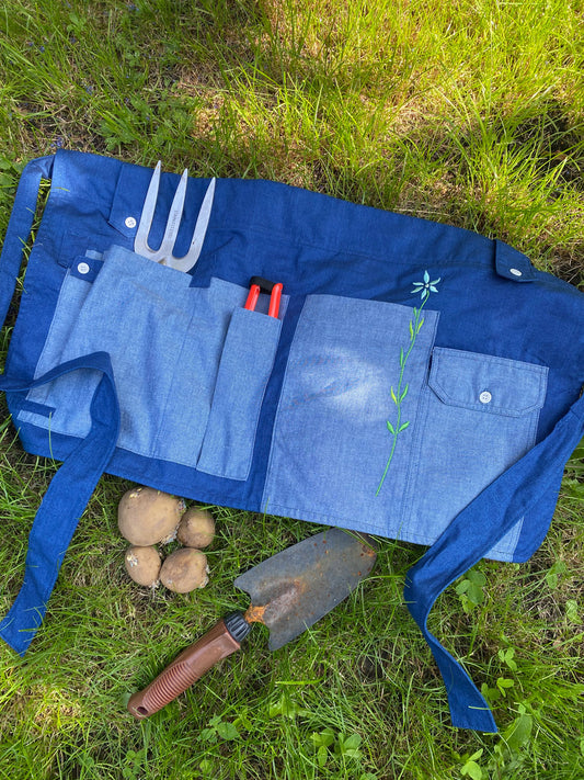 Saywood's Gardener's Tool Belt in Japanese Denim, with garden tools including fork, trowel, secateurs, and potatoes on the grass