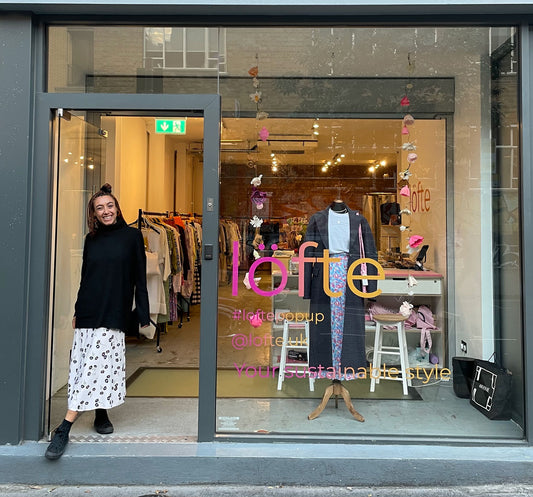 Lofte's first sustainable pop up shop. The pink/ orange Lofte branding is on the window, with a mannequin dressed in the centre of the window. A customer smiles in the doorway to the store