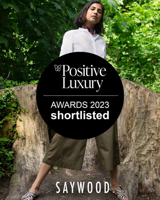 Positive Luxury Awards 2023 Shortlisted badge, over image of Saywood model in the Marie A-line recycled cotton white blouse, worn with the khaki wide leg trouser Amelia style
