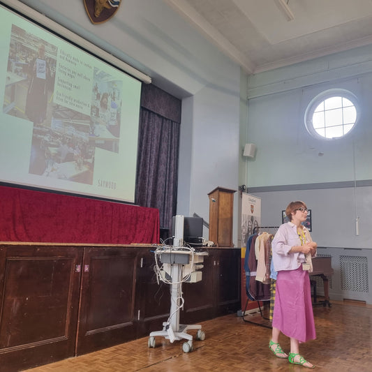 SAYWOOD founder, Harriet, giving a sustainable fashion talk in a school hall with a presentation on a screen above the stage.