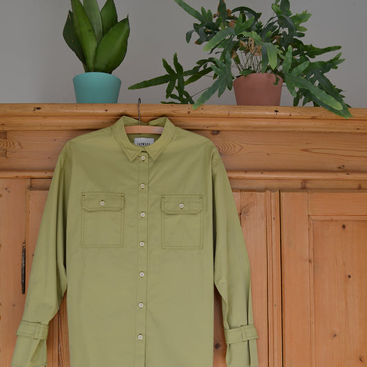 Saywood Zadie Boyfriend Shirt in olive hanging on an old french pine wardrobe, with plants sitting atop. For blog post about the meaning of sustainable fashion.