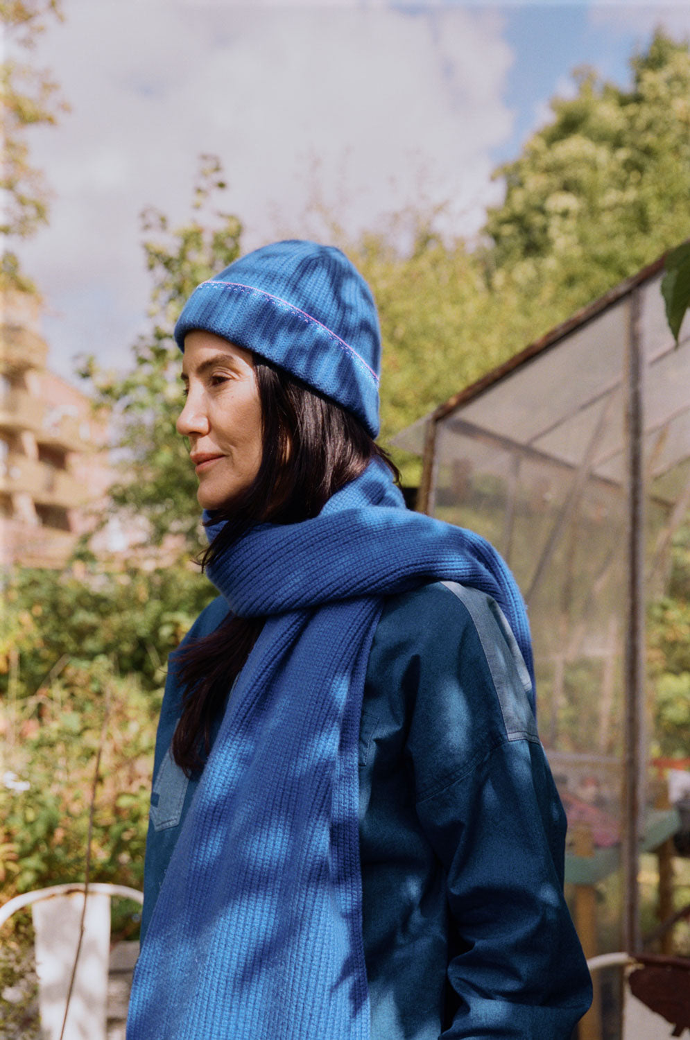 Person wearing a blue beanie and scarf outdoors with greenery in the background