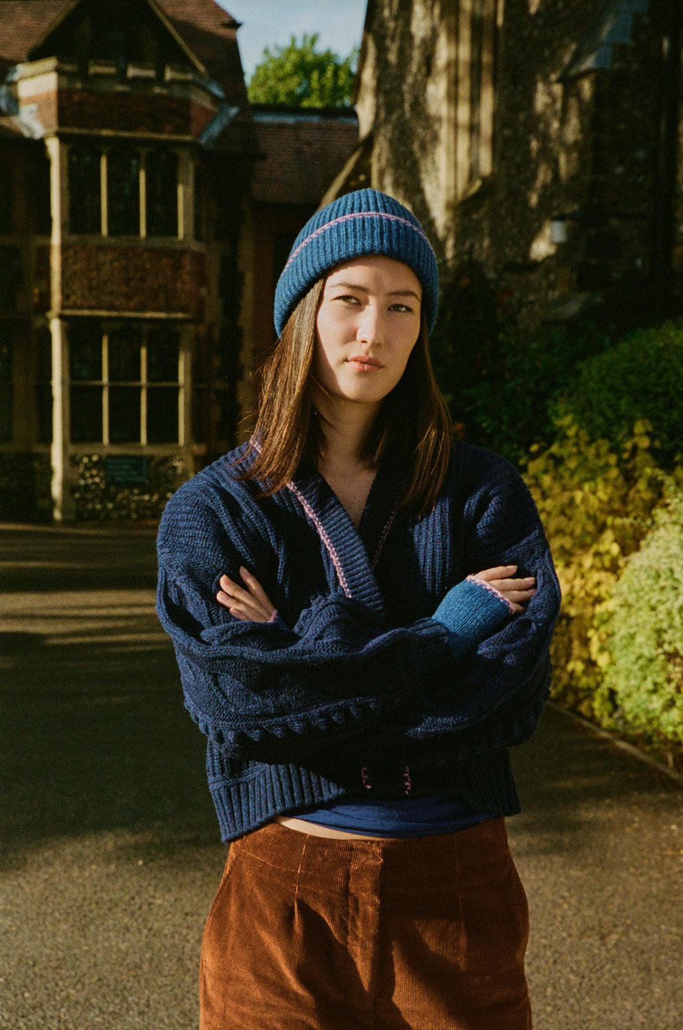 Frida navy chunky-knit cardigan with textured sleeves and blue contrast cuffs, worn with caramel corduroy trousers and a blue beanie.