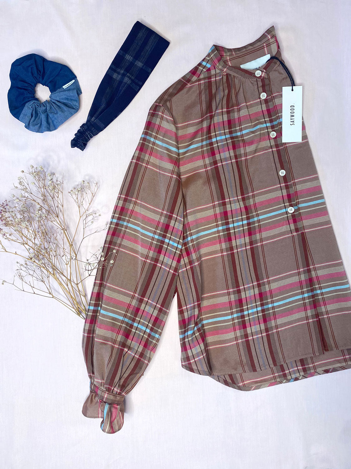 Pink check silky blouse with gathered cuffs lays next to a navy check headband and patchwork denim scrunchie.