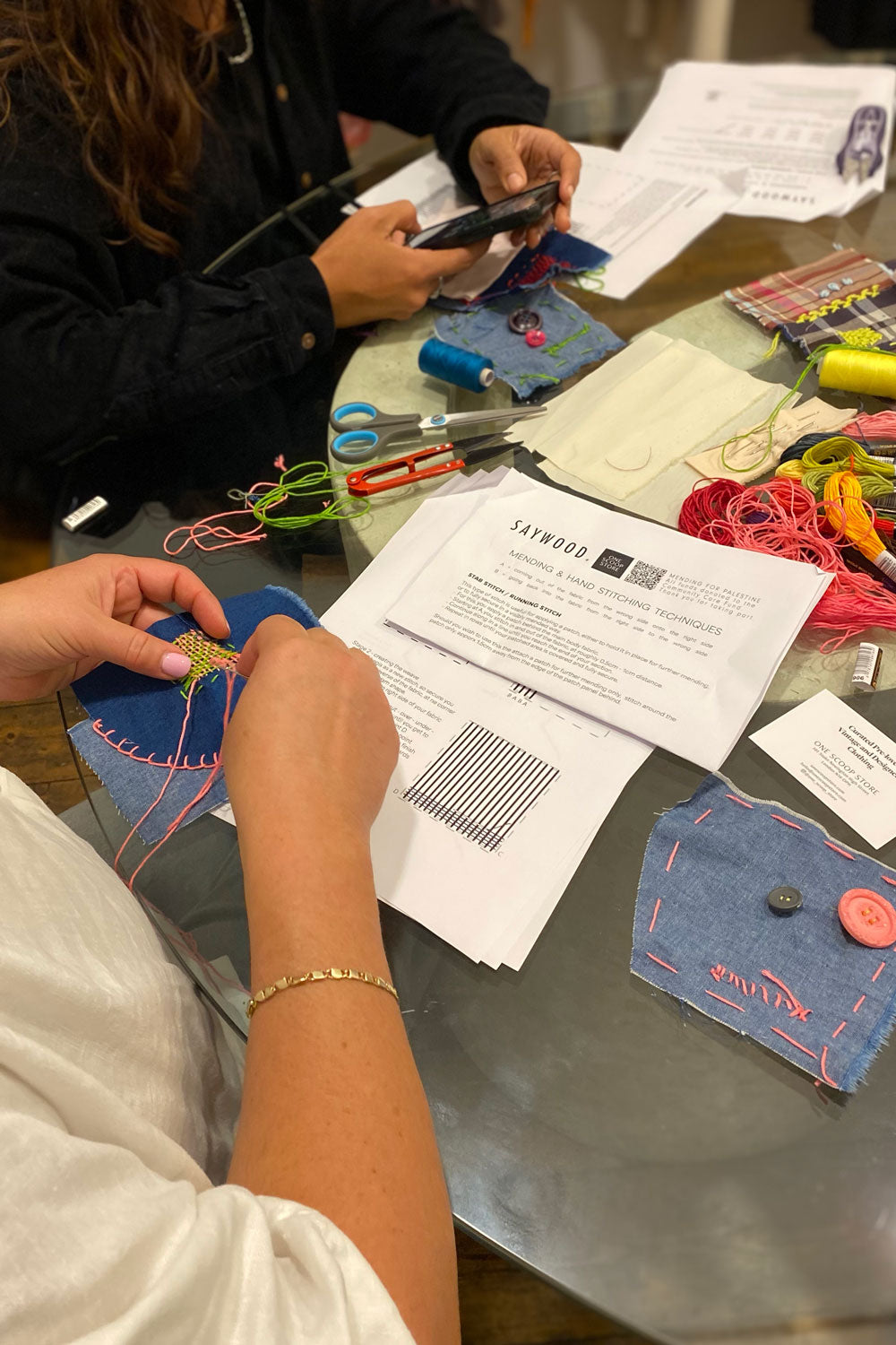 Participants learning hand sewing techniques at mending workshop table