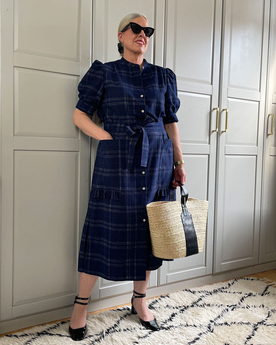 Stylist Emily Fitch-Miller wears Saywood's Rosa Puff Sleeve Dress in navy check, with a low heeled sandal, sunglasses and basket bag for summer