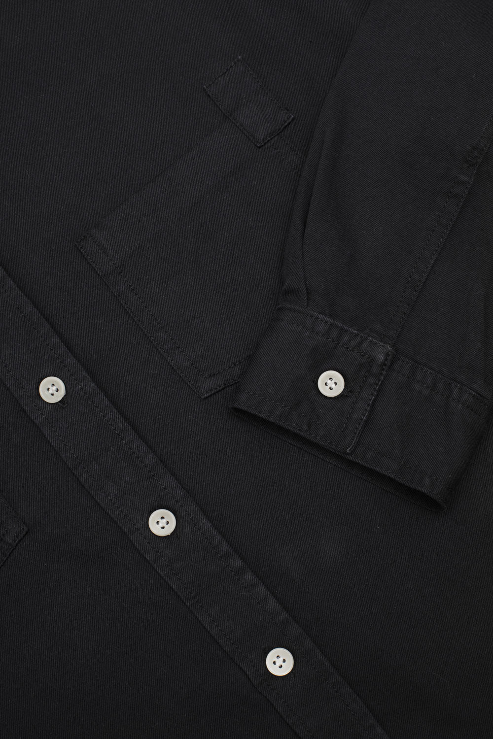 Close-up of a black shirt with natural corozo buttons on a plain background