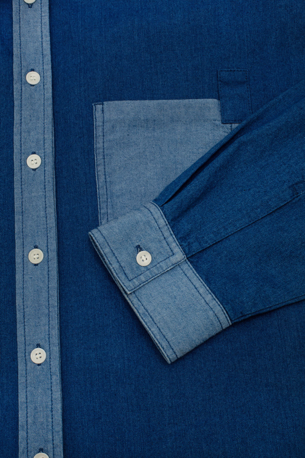 Close-up of a blue denim shirt with buttons and contrast placket, cuffs and pocket details