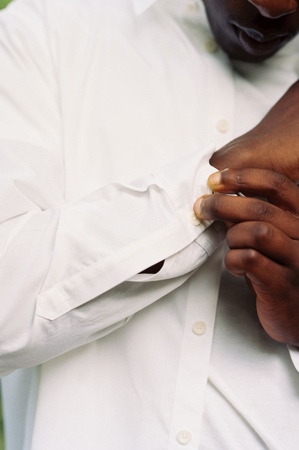 Close up of a black man doing up his shirt cuffs. He is wearing Saywood's Eddy Men's Classic White Shirt with long sleeves, worn open over a white t-shirt.