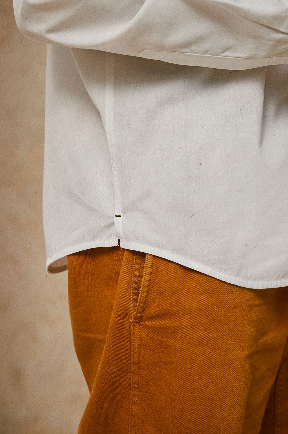 Close up of the cuff details of Saywood's Eddy Mens Classic White Shirt. Worn with tobacco trousers just visible. The contrast colour bar tack at the hem side seam can be seen, with the man standing side on.