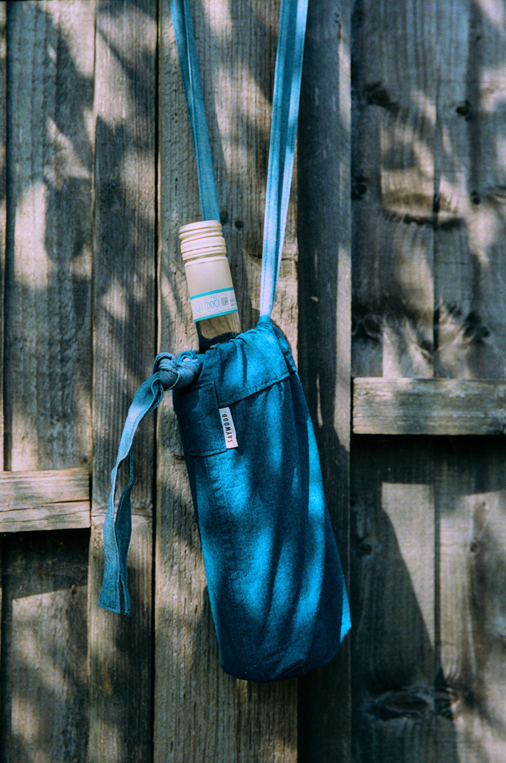 Japanese Denim Mini Bag / Bottle Bag, with a wine bottle in, hanging on a wooden fence post.