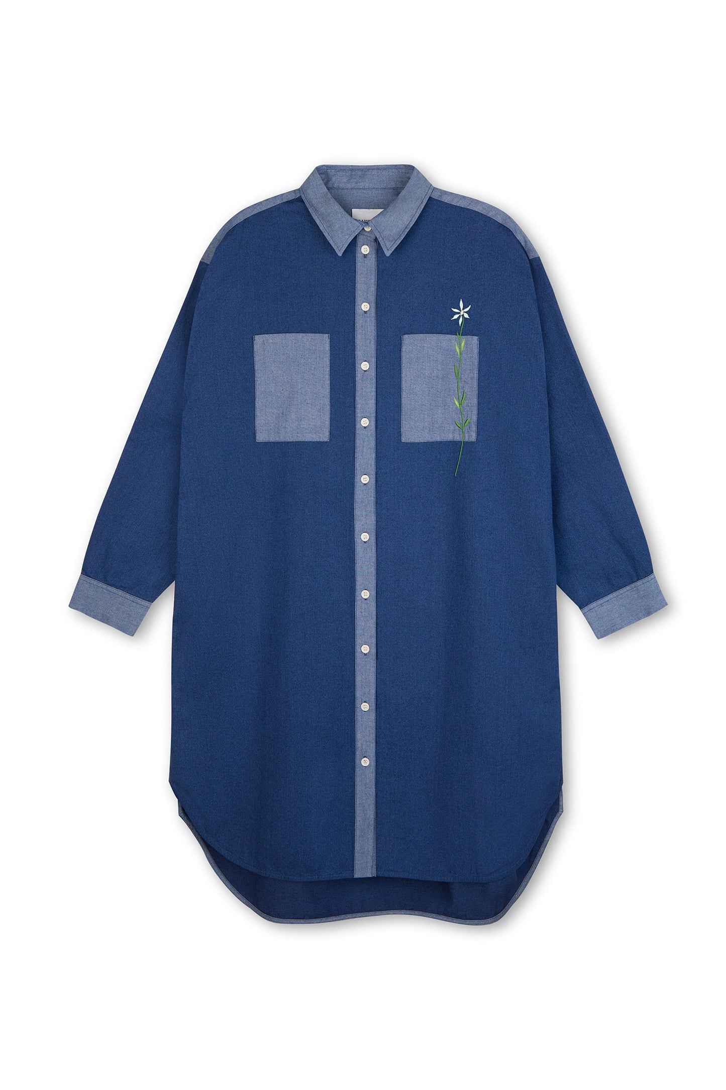 Womens Oversized Shirtdress in Japanese Denim, with lighter wash contrasting collar, placket, cuffs and pocket. Right pocket has a flower embroidery positioned through the pocket. Dress is on a white background.