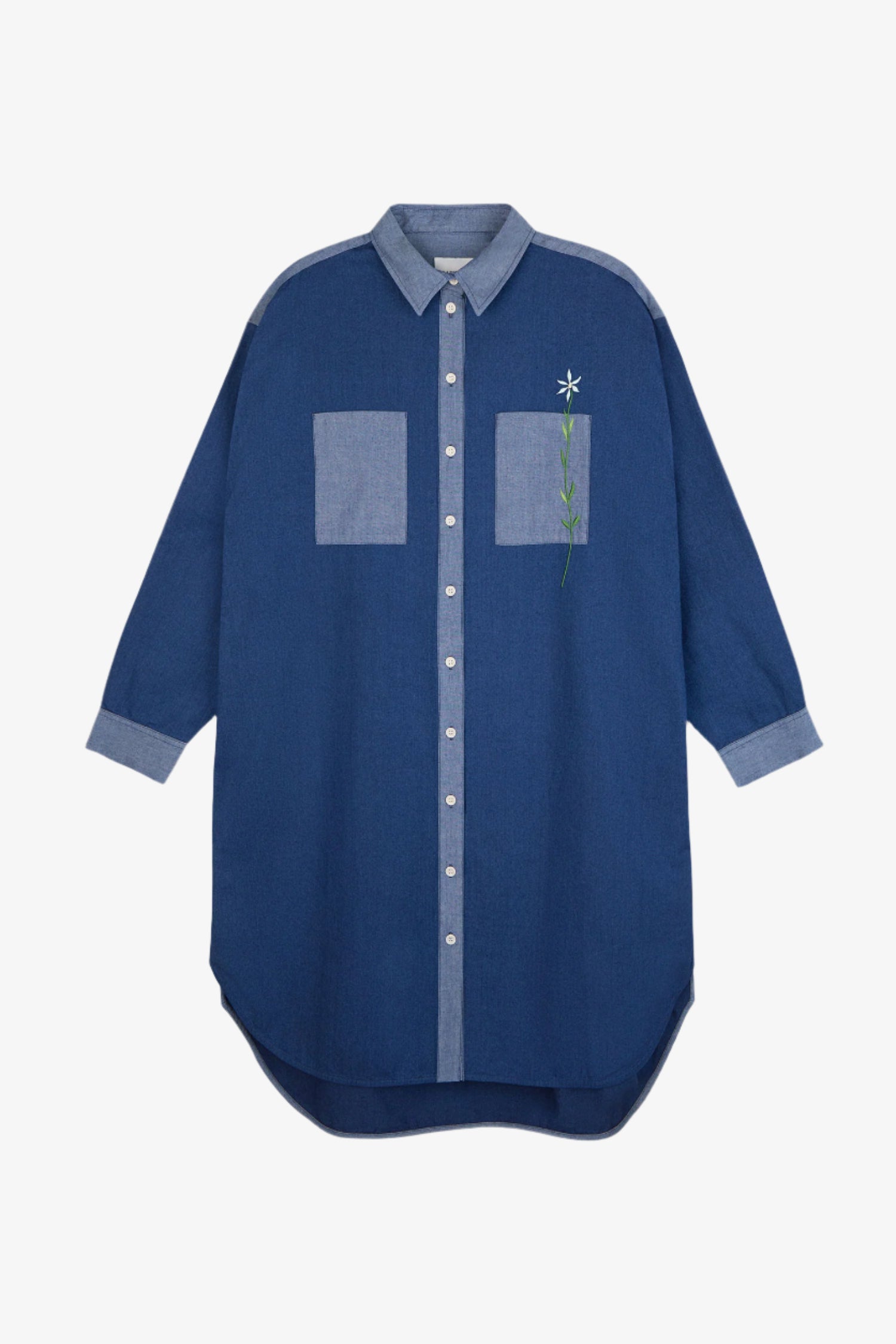 Womens Oversized Shirtdress in Japanese Denim, with lighter wash contrasting collar, placket, cuffs and pocket. Right pocket has a flower embroidery positioned through the pocket. Dress is on a white background.