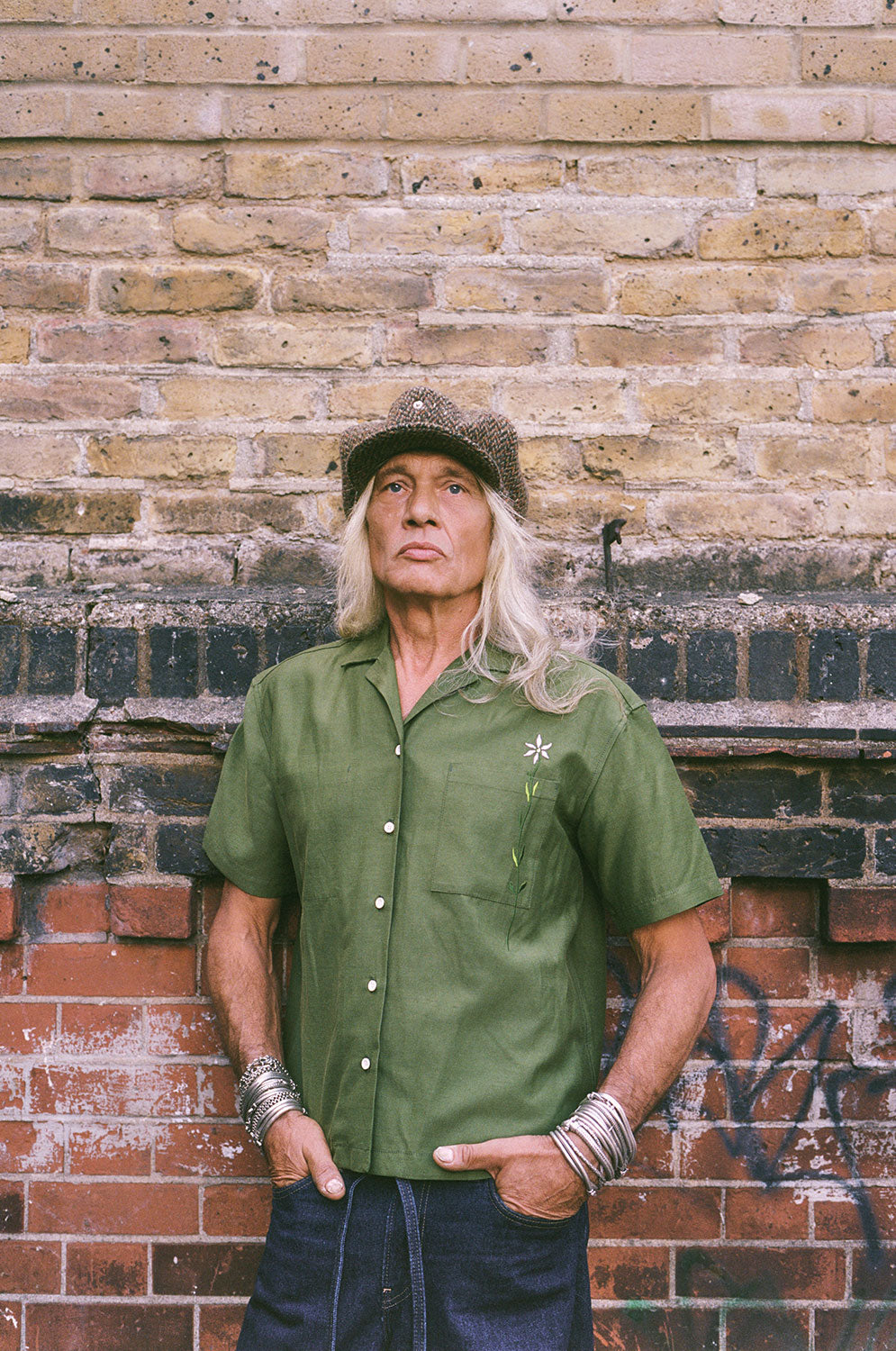 Man wearing a green shirt and hat against a brick wall