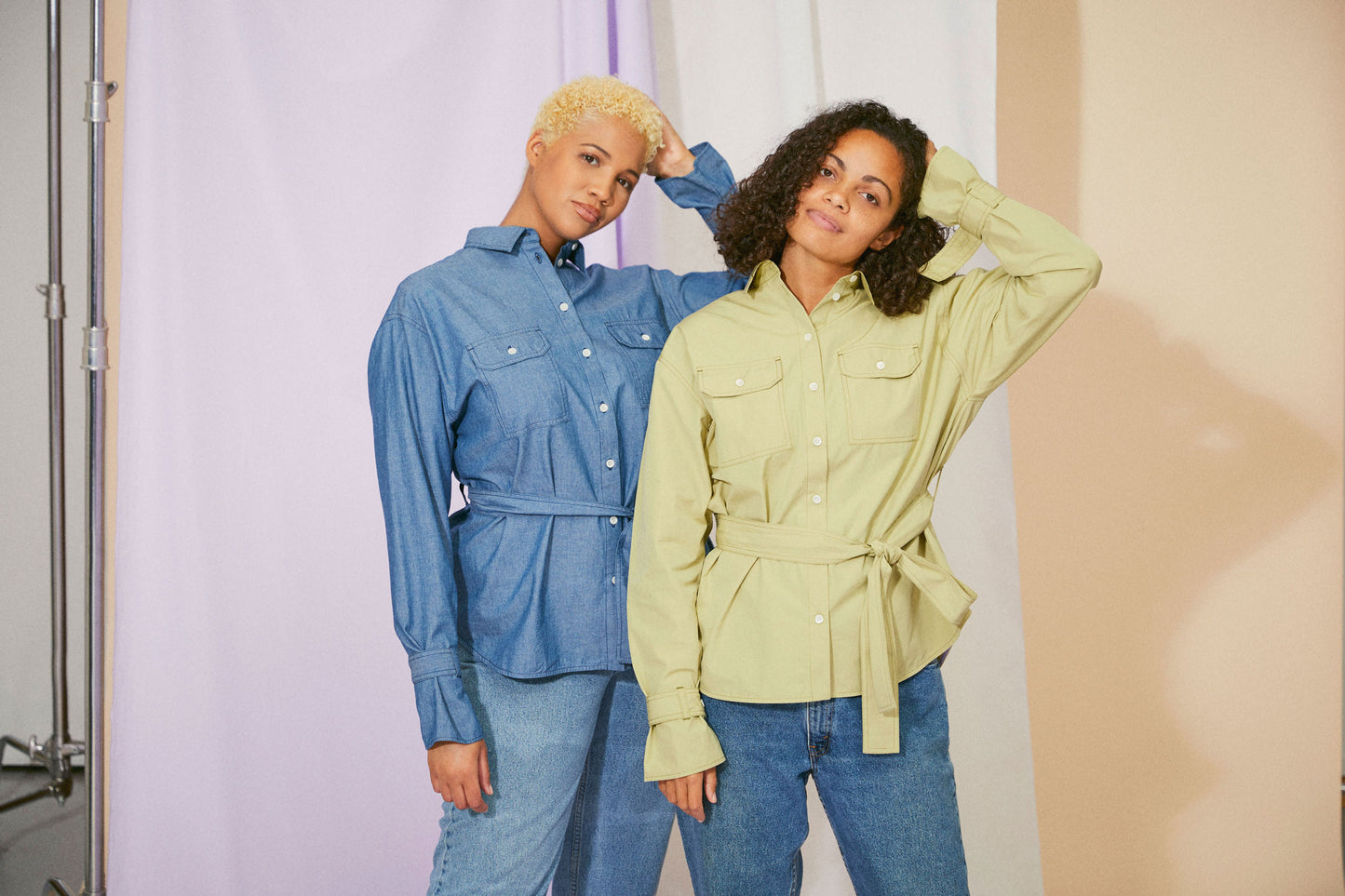 Womens Oversized Shirt in khaki olive, with detachable tie belt and safari styling details. Belted cuffs for sleeve details and utility patch pockets. Zadie Boyfriend Shirt by Saywood. Two models stand side by side. The model on the right wears the olive shirt. The model on the left wears the denim oversized shirt colourway.