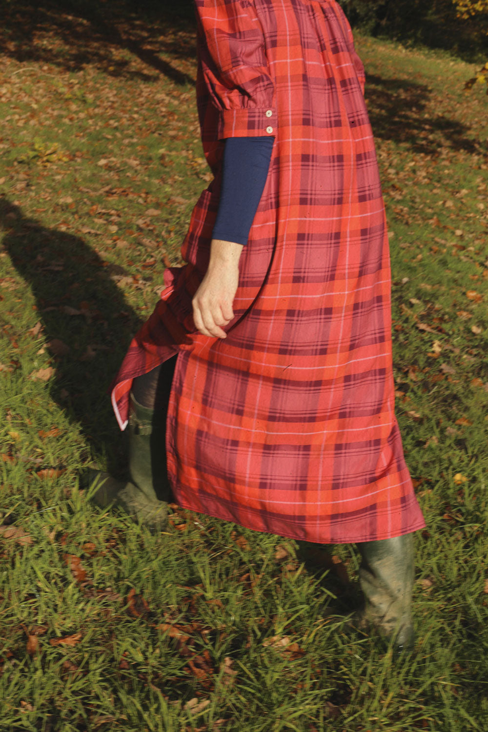 Person wearing a red plaid dress walking on grass in wellington boots
