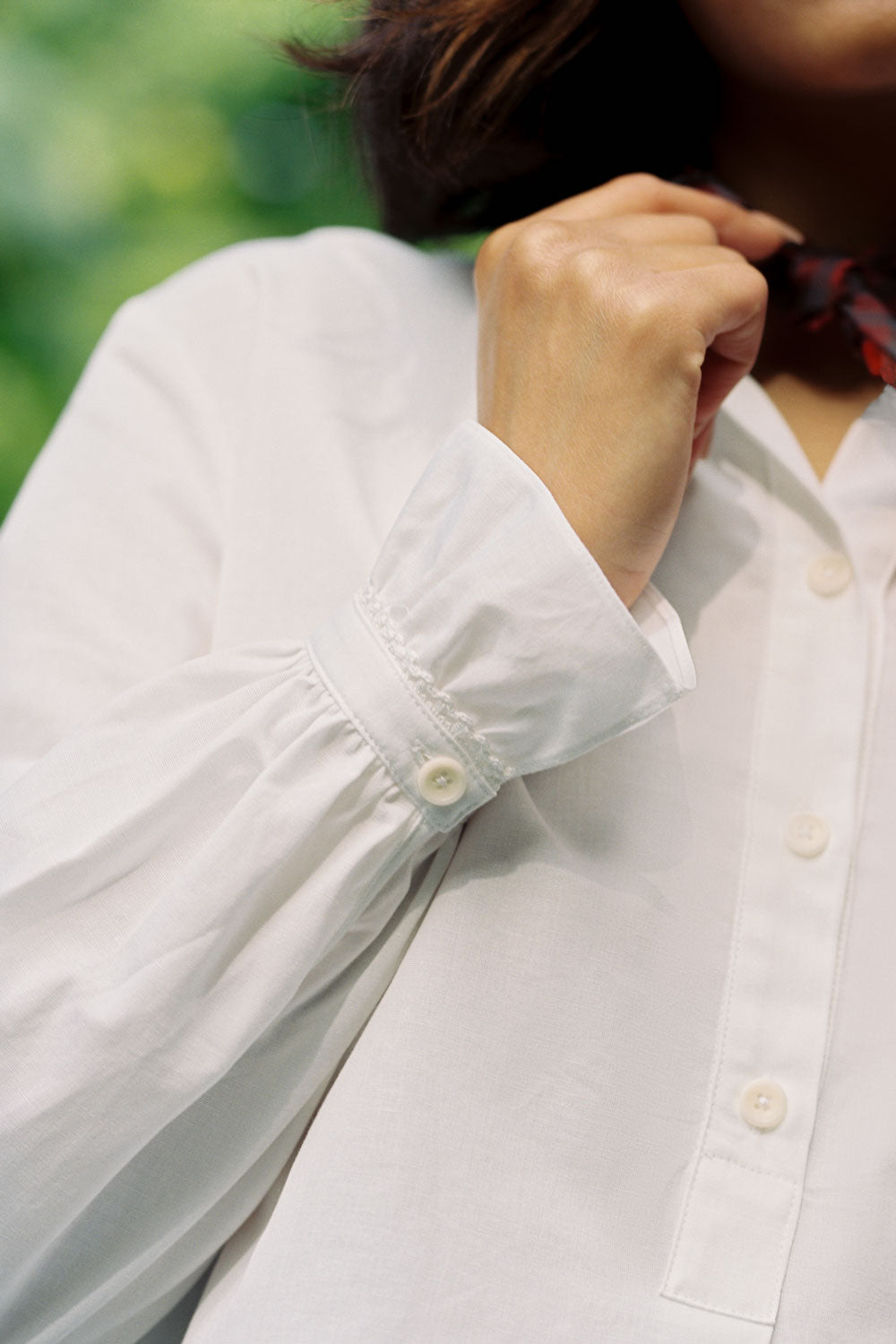 Close up detail shot f the gathered cuff with lace trim at the frill, of the Marie A-line Gathered Neck Blouse by Saywood. Worn by a model who is touching a red check neck tie around her neck.