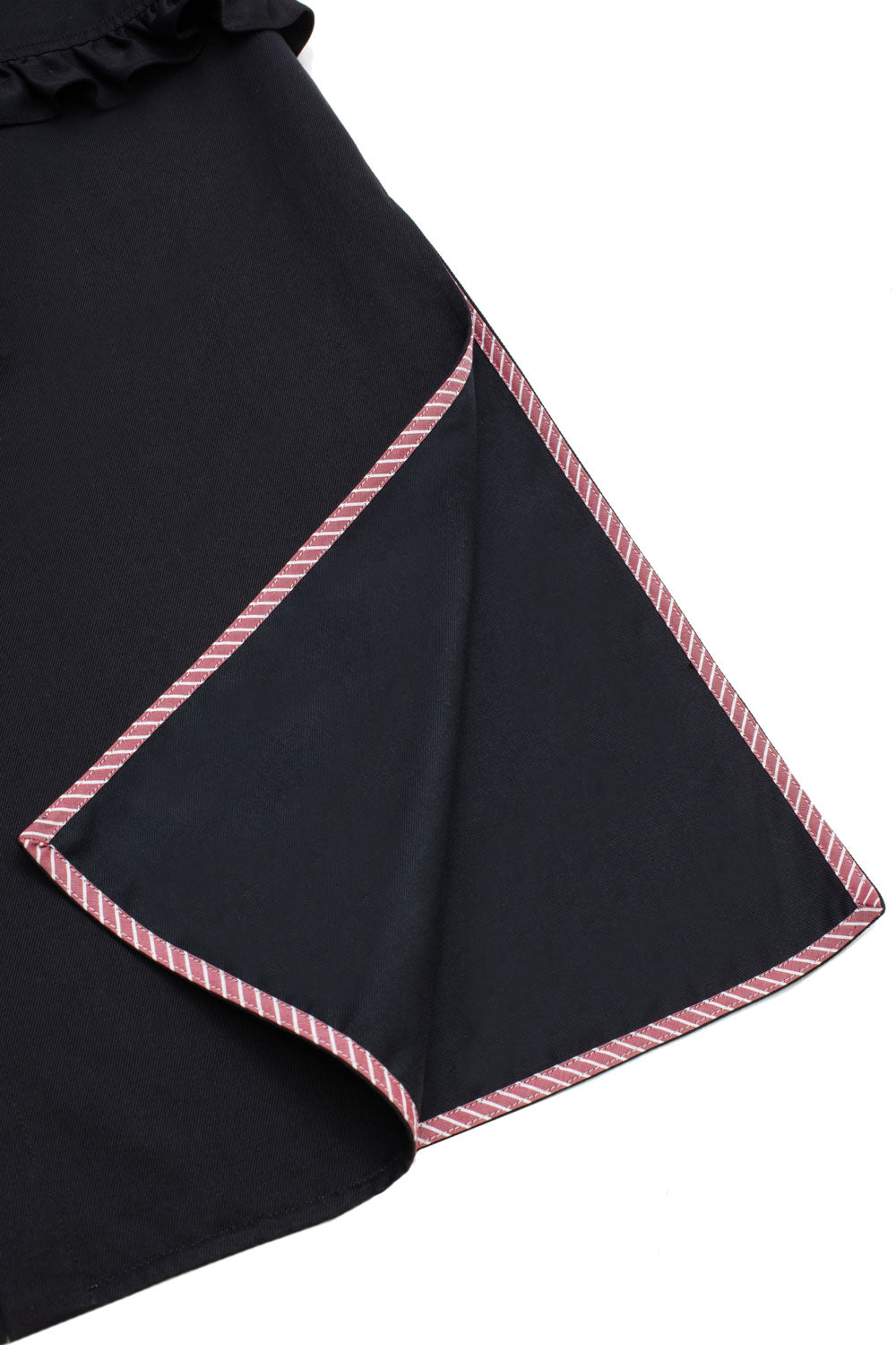 Close up of the hem side splits on the Rosa Puff Sleeve Shirtdress in black Japanese denim. One split is folded back and the red and white stripe internal hem bind detail can be seen. The image is a flat shot on a what background.