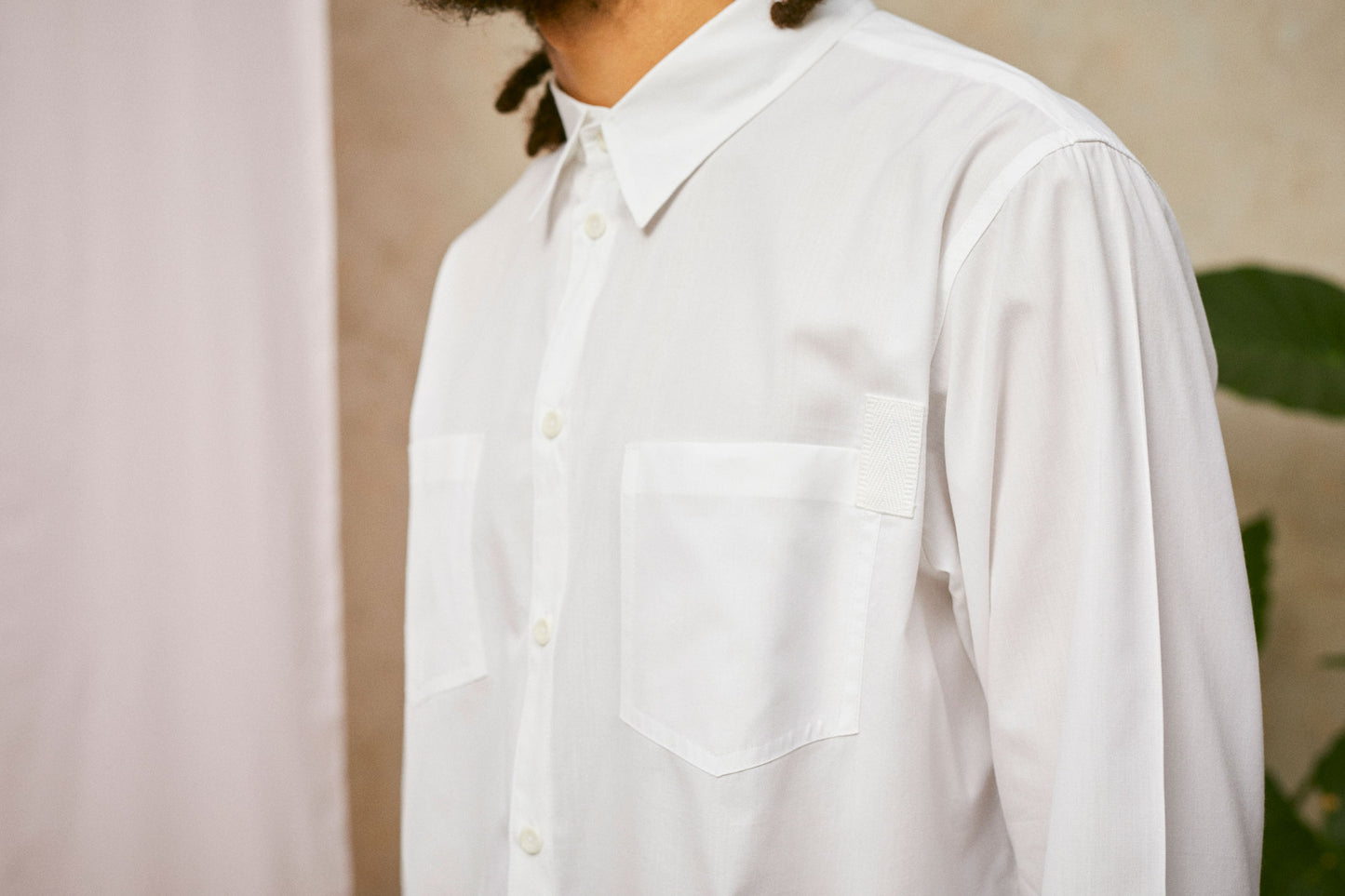 Close up of Saywood's Eddy Mens mens white Shirt showing the patch pockets with cotton herringbone tape on one corner. A drop of pink fabric can be seen in the background.