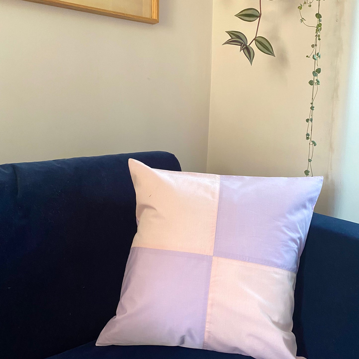 Patchwork cushion, harlequin style cushion, in pink and lilac. Sustainable Homeware, position on a navy sofa against a white wall with green leafy house plants hanging behind
