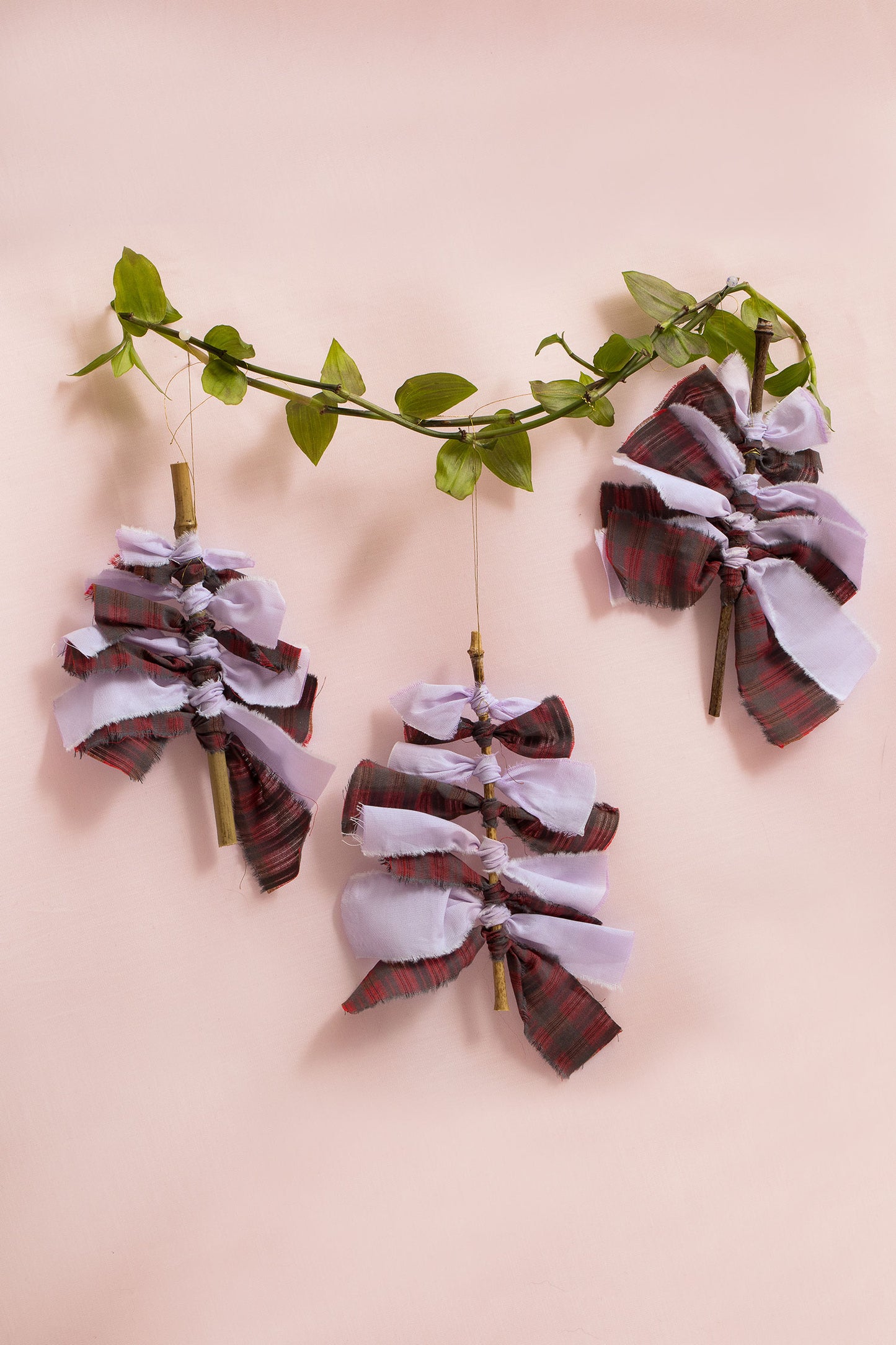 Sustainable Christmas Decorations from Saywood. Christmas tree with red check and lilac fabric tied round bamboo stick with gold thread to hang on the tree. Eco-friendly Christmas decoration