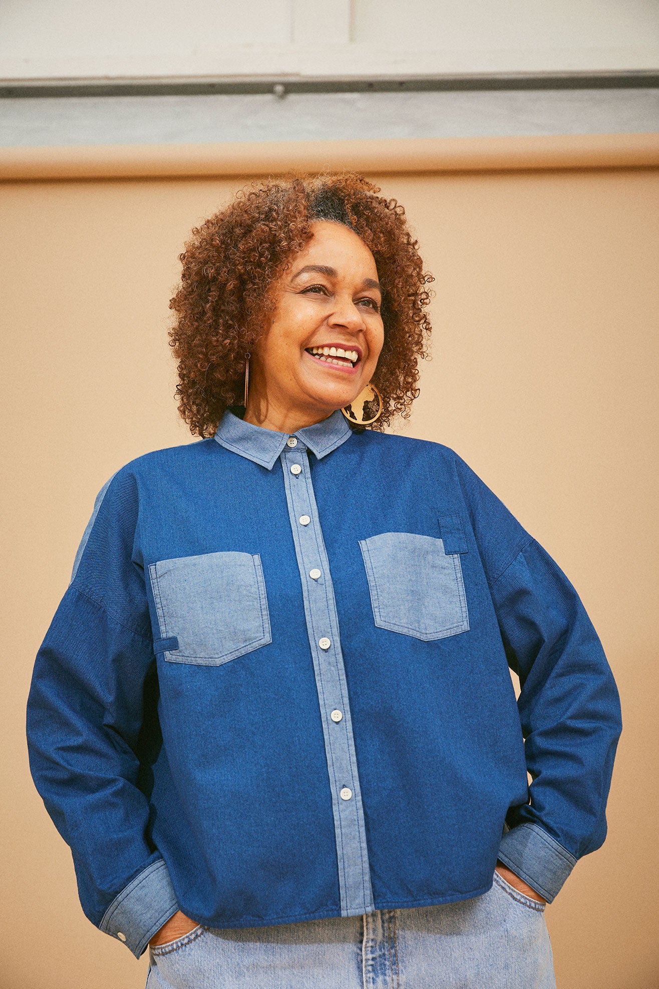 Model stands in front of coffee background. She wears Saywood's Japanese Denim Lela Patchwork Shirt, with light wash contrast cuffs, pockets and collar. Worn with jeans.